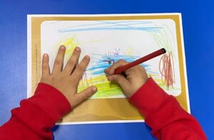 child's hands drawing with coloured pencils