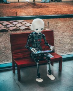 A robot sitting on a park bench typing on a laptop.