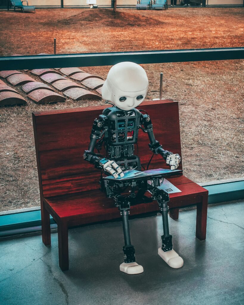 A robot sitting on a park bench typing on a laptop.