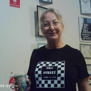 Volunteer Tina wears a ska street shirt, smiles holding a coffee cup